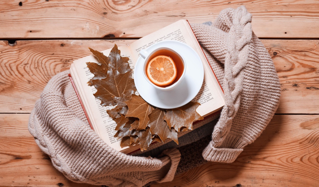 Чашка чая с лимоном на столе с книгой и теплой кофтой