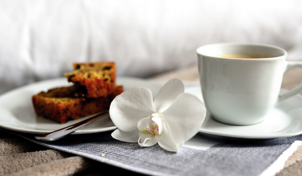 Чашка кофе на столе с цветком орхидеи и кусочками кекса 