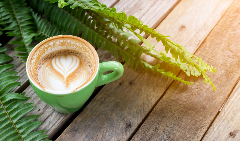 Чашка вкусного капучино  на столе с листьями папоротника