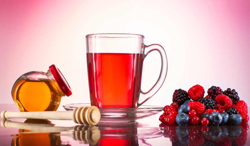 Чашка чая с медом на столе с ягодами