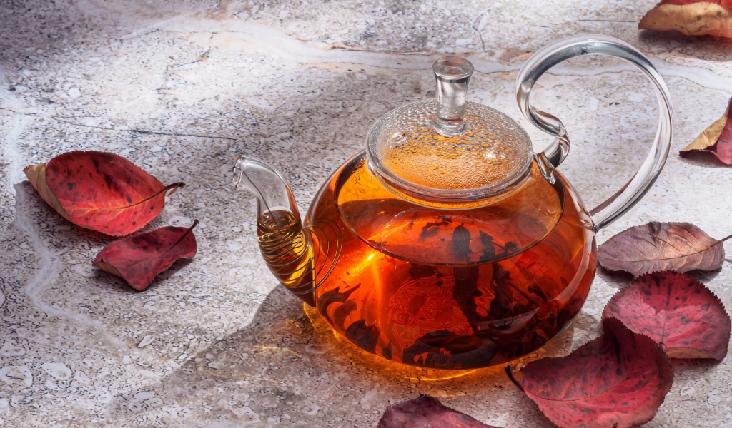 Стеклянный чайник на столе с листьями