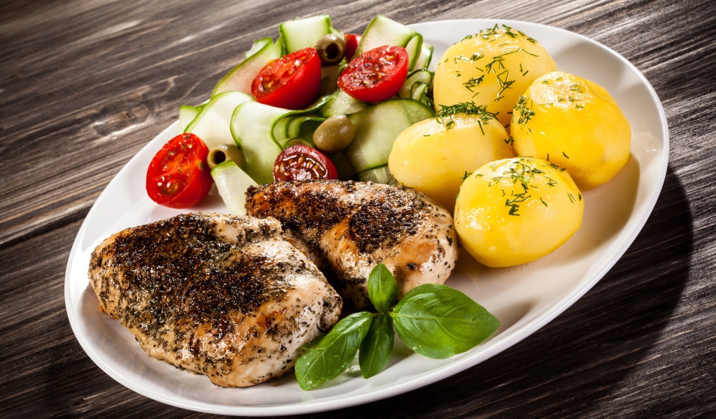 Куски курицы на тарелке с картофелем, помидорами и кабачком 