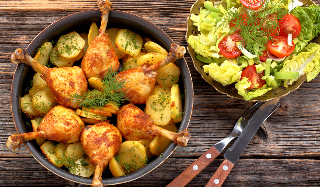 Fried chicken legs with potatoes on a table with salad