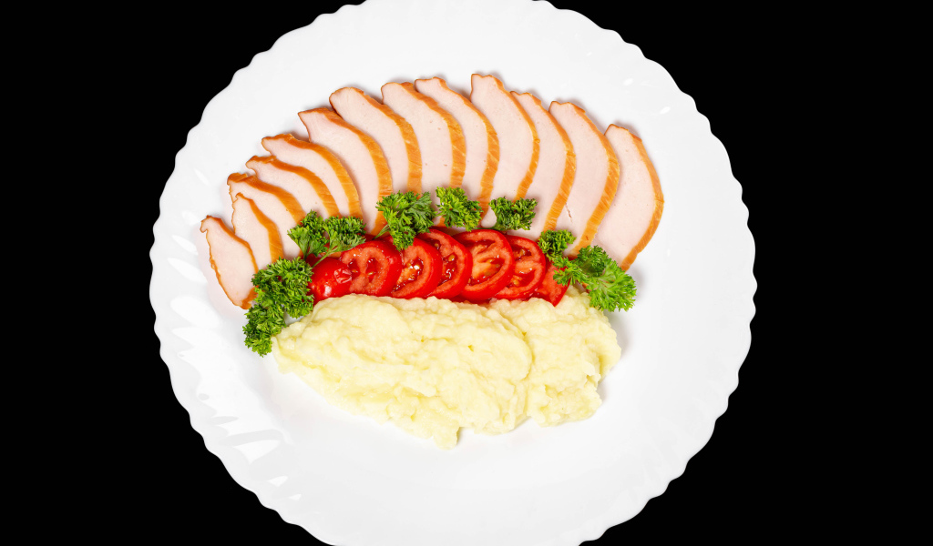 Ham on a large white plate with potatoes and tomatoes