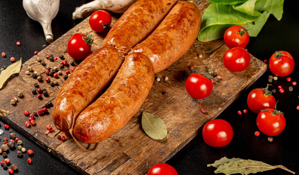 Мясные колбаски на доске с овощами