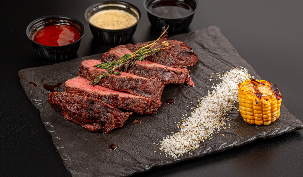 Кусок запеченного мяса на доске с кукурузой и специями 