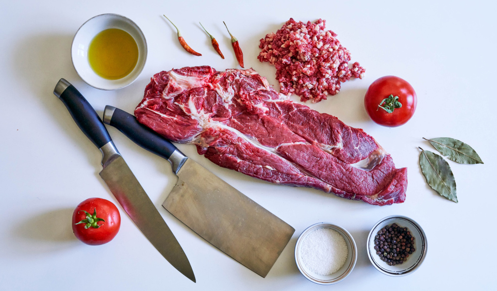 Кусок мяса со специями и ножами на столе 