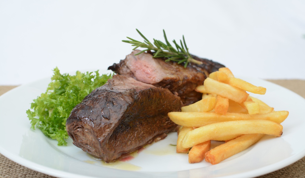 Два куска мяса на тарелке с картофелем фри 