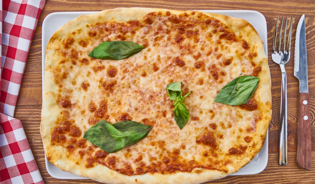 Пицца с сыром и листьями базилика на столе со столовыми приборами