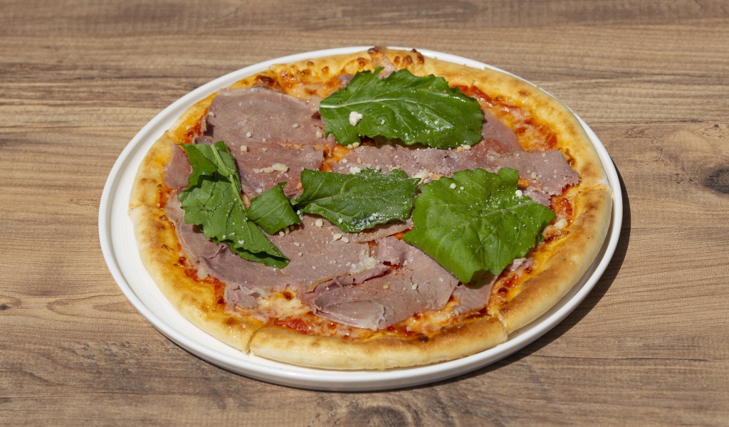 Пицца с кусочками мяса и зеленью на столе