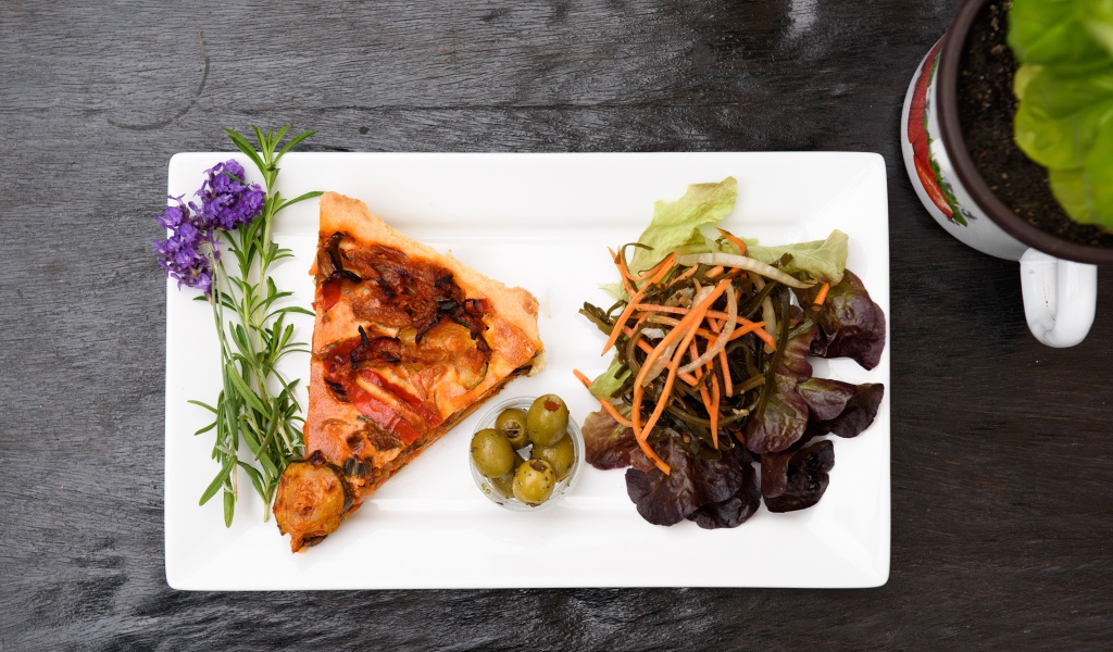 Кусок пиццы с салатом и оливками на белой тарелке