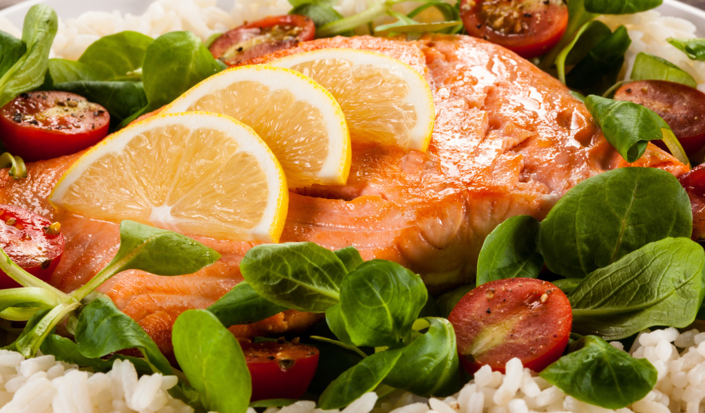 Кусок запеченной красной рыбы на тарелке с лимоном, рисом, базиликом и помидорами