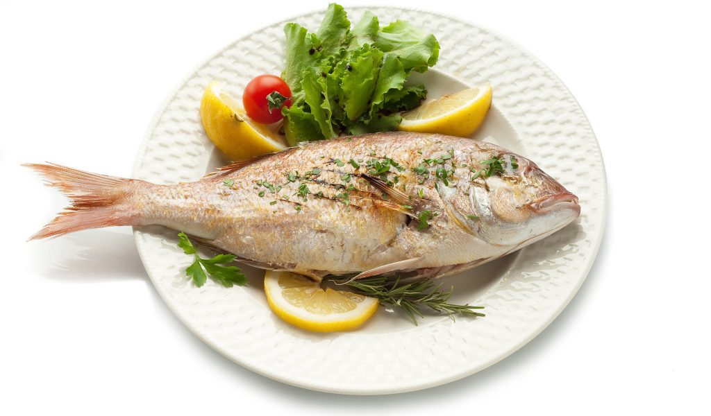 Запеченная рыба на тарелке с зеленью и лимоном