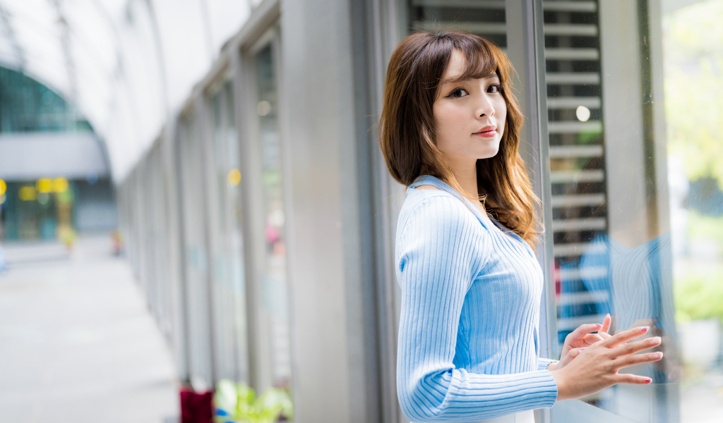 Красивая девушка азиатка в в голубой кофте стоит уокна