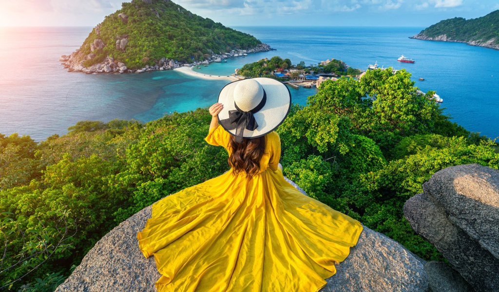 Девушка в красивом желтом платье сидит на камне с видом на море