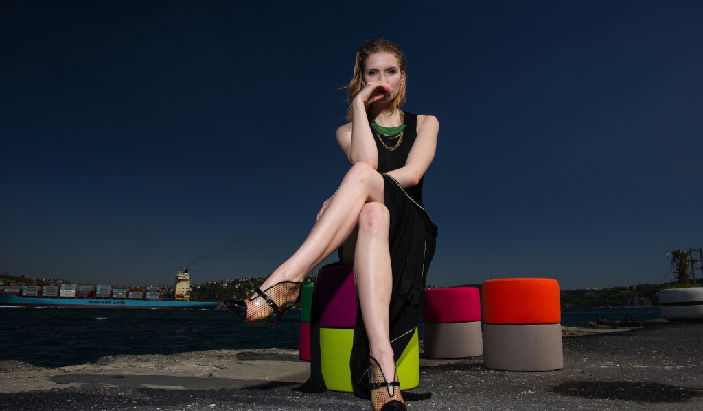 Девушка в черном платье сидит у воды