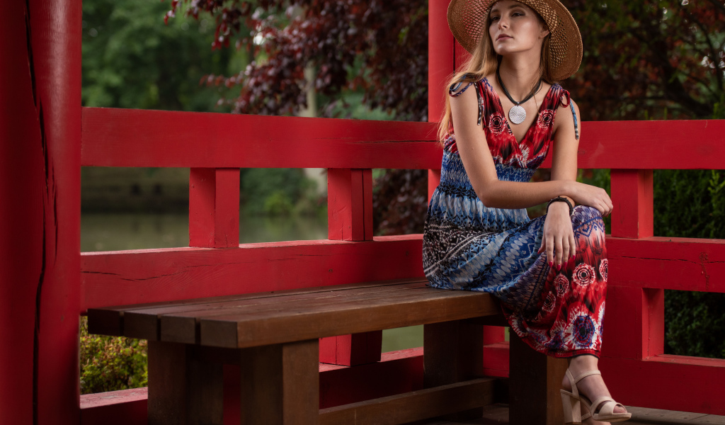 Молодая девушка в платье сидит на лавке 