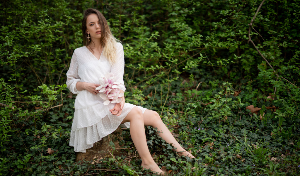 Молодая девушка в белом платье сидит на камне в лесу 