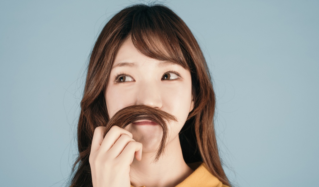 Девушка азиатка закрыла лицо волосами на сером фоне 