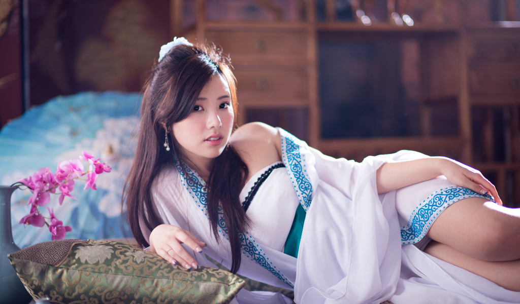 Девушка азиатка в красивом платье лежит на кровати 