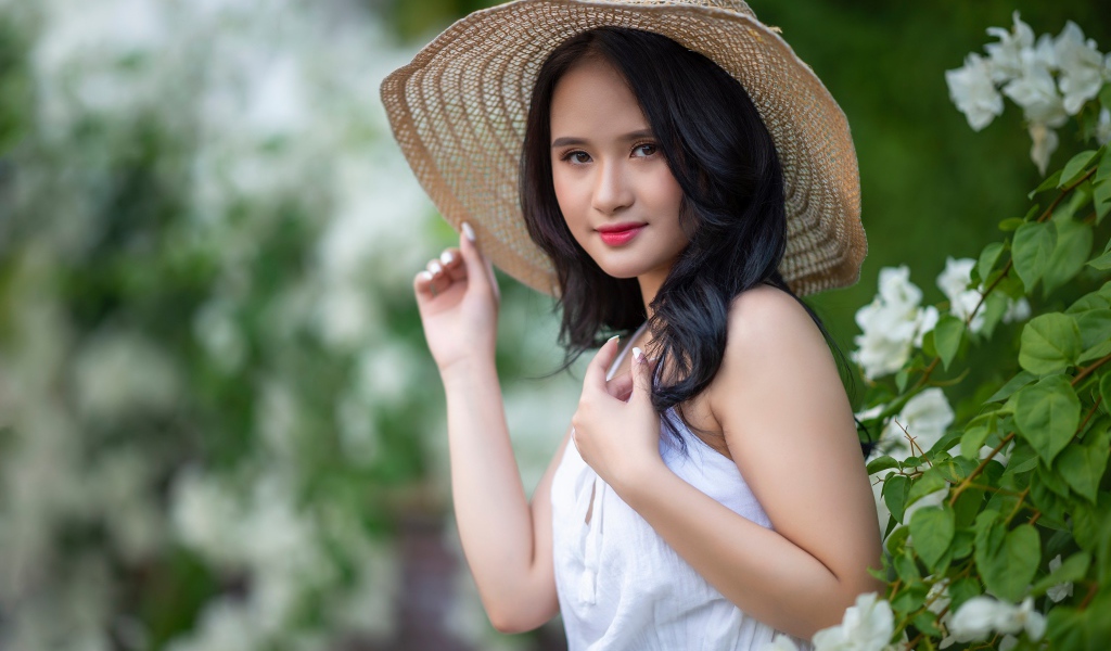 Девушка азиатка в большой шляпе у зеленого куста