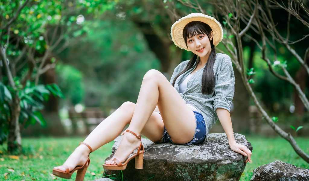 Девушка азиатка в шляпе сидит на камне