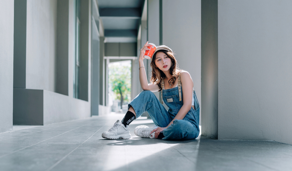 Девушка азиатка в синем комбинезоне с кофе в руке 