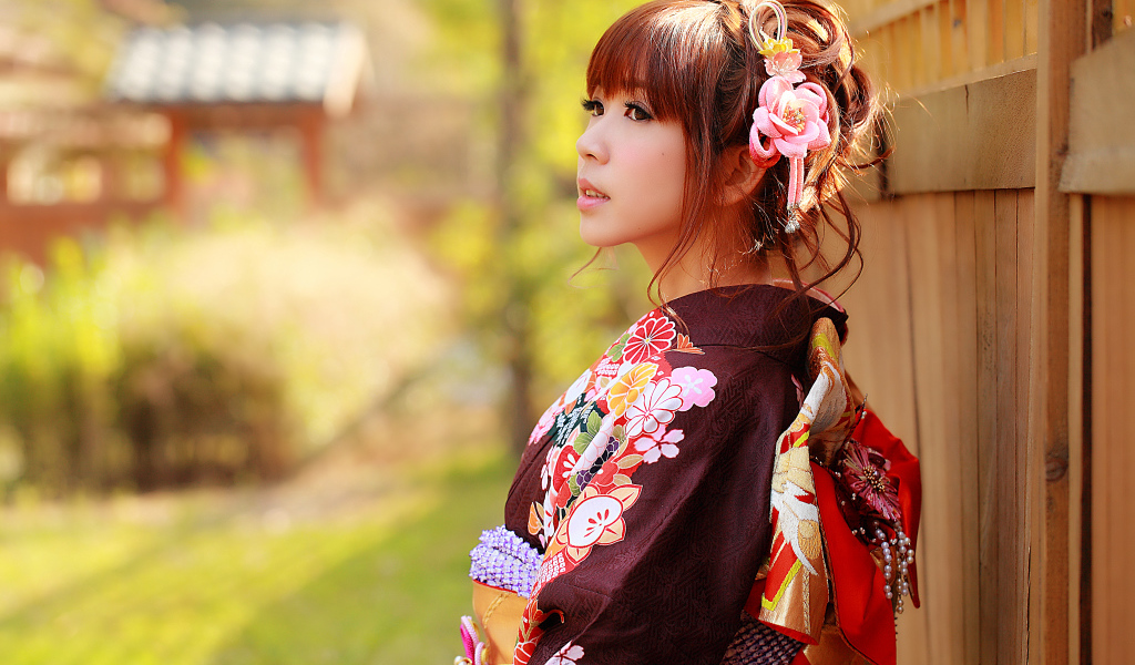 Девушка азиатка в кимоно стоит у забора 