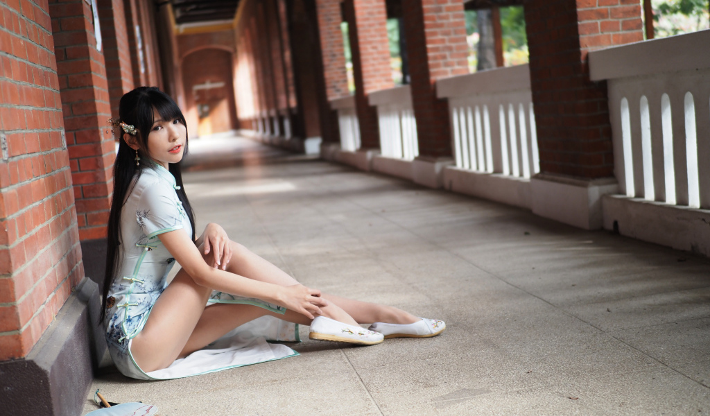 Девушка азиатка сидит на холодном полу у стены