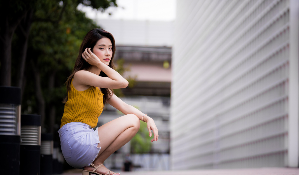 Девушка азиатка сидит на корточках у стены