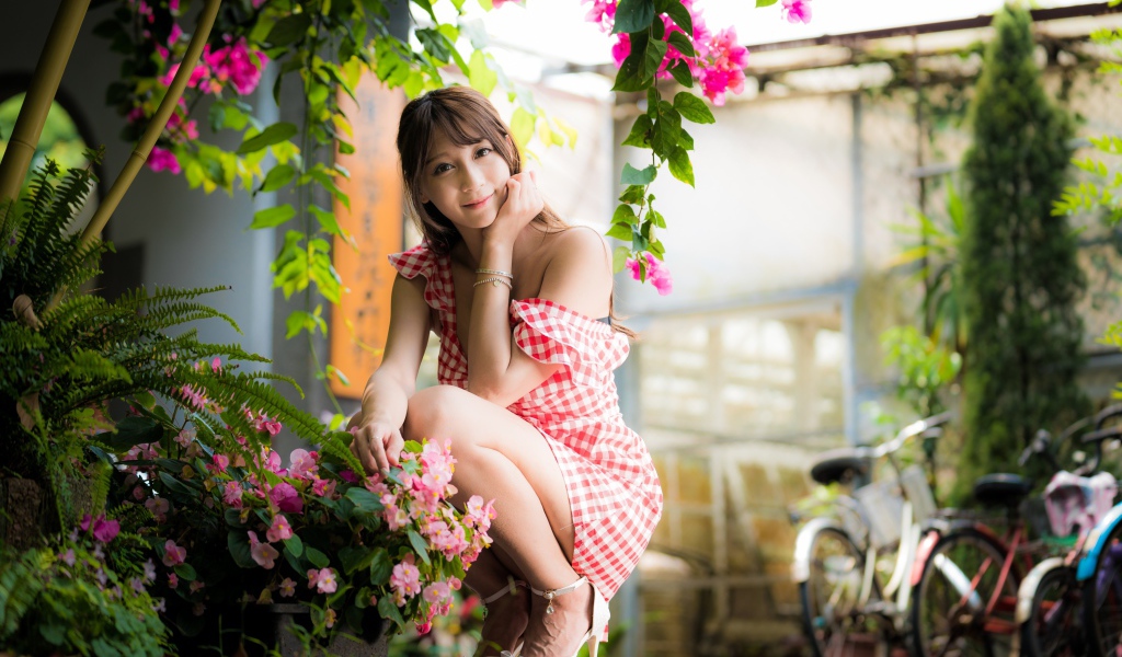 Девушка азиатка сидит на корточках у розового цветка