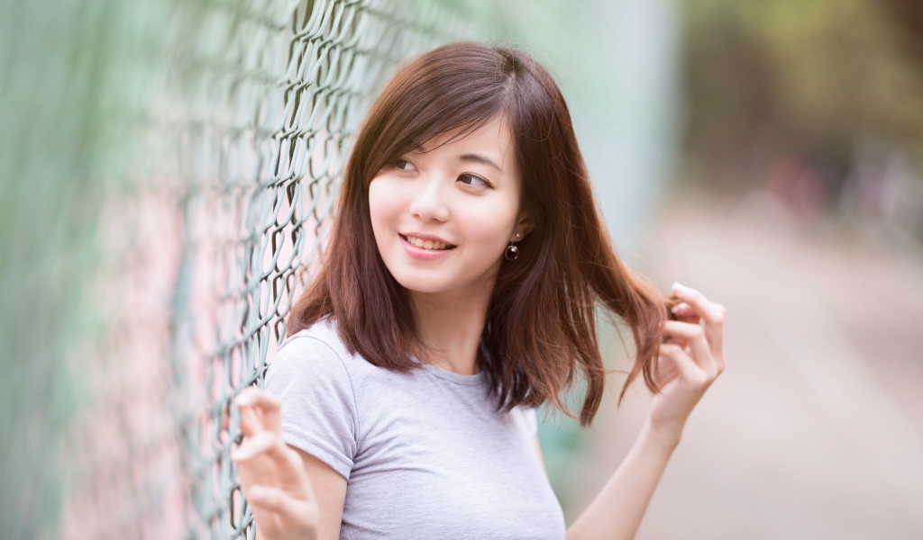 Девушка азиатка с милой улыбкой стоит у сетки 