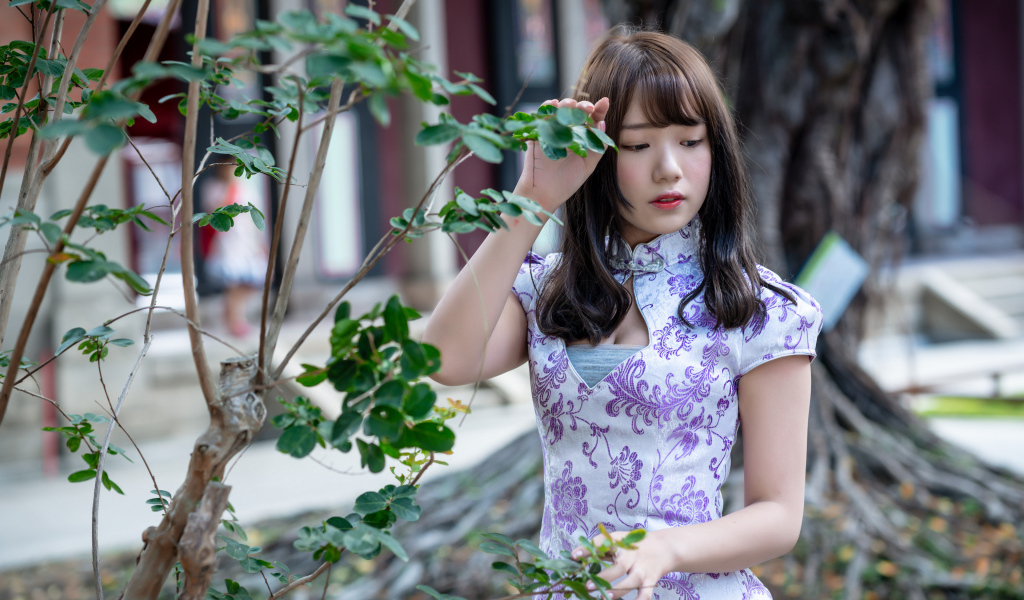 Красивая девушка азиатка в платье стоит у дерева 