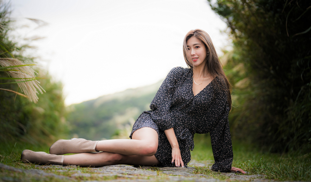 Красивая девушка азиатка в платье лежит на земле 