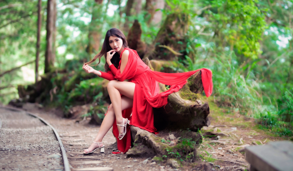 Красивая азиатка в красном платье сидит на дереве 