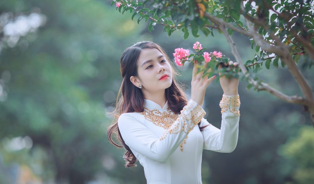 Красивая азиатка в белом платье у ветки с розовыми цветами