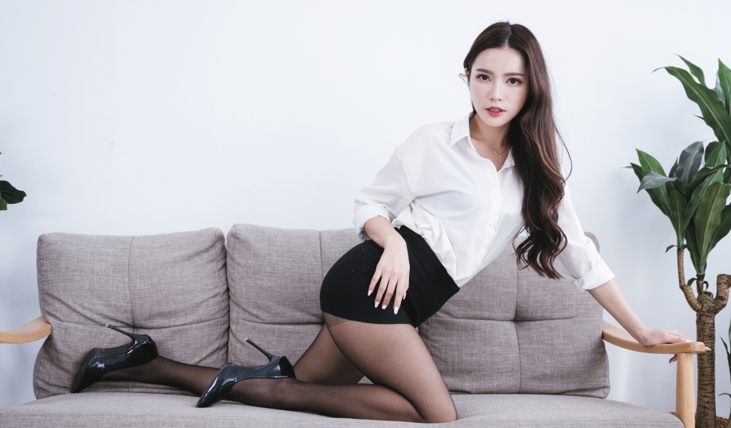Красивая азиатка в белой рубашке на диване