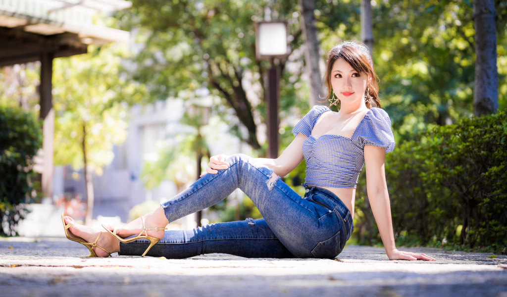 Красивая азиатка в джинсах сидит на земле