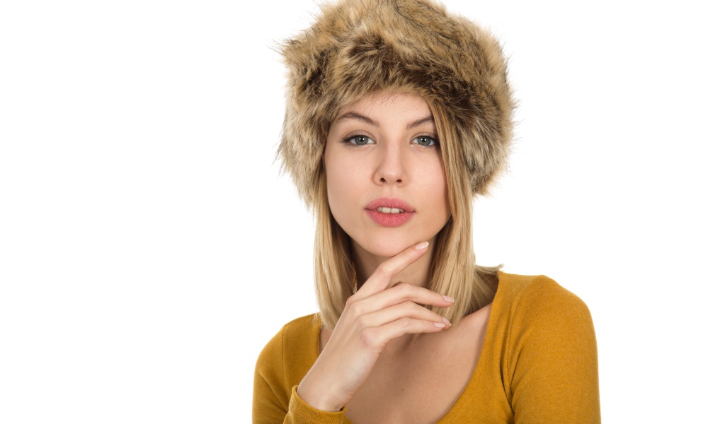 Красивая девушка блондинка в меховой шапке на белом фоне 