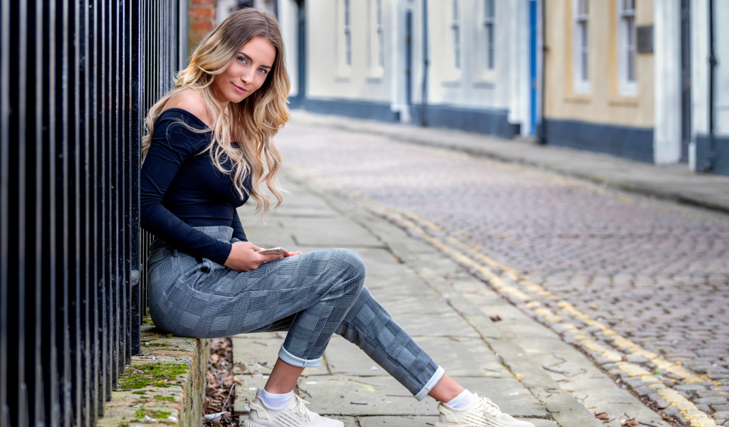 Красивая девушка блондинка сидит у забора