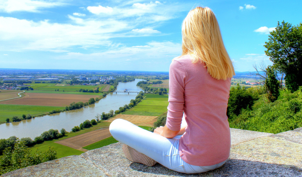 Красивая блондинка сидит на камне у реки