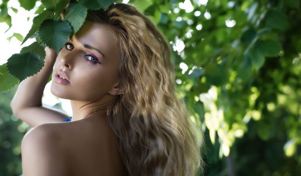 Красивая голубоглазая блондинка у ветки с зелеными листьями