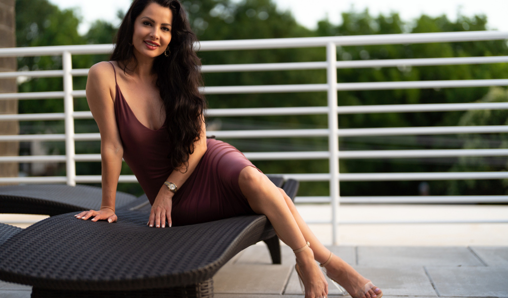 Красивая брюнетка в платье сидит на диване 