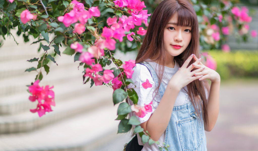 Красивая милая азиатка стоит у куста с розовыми цветами
