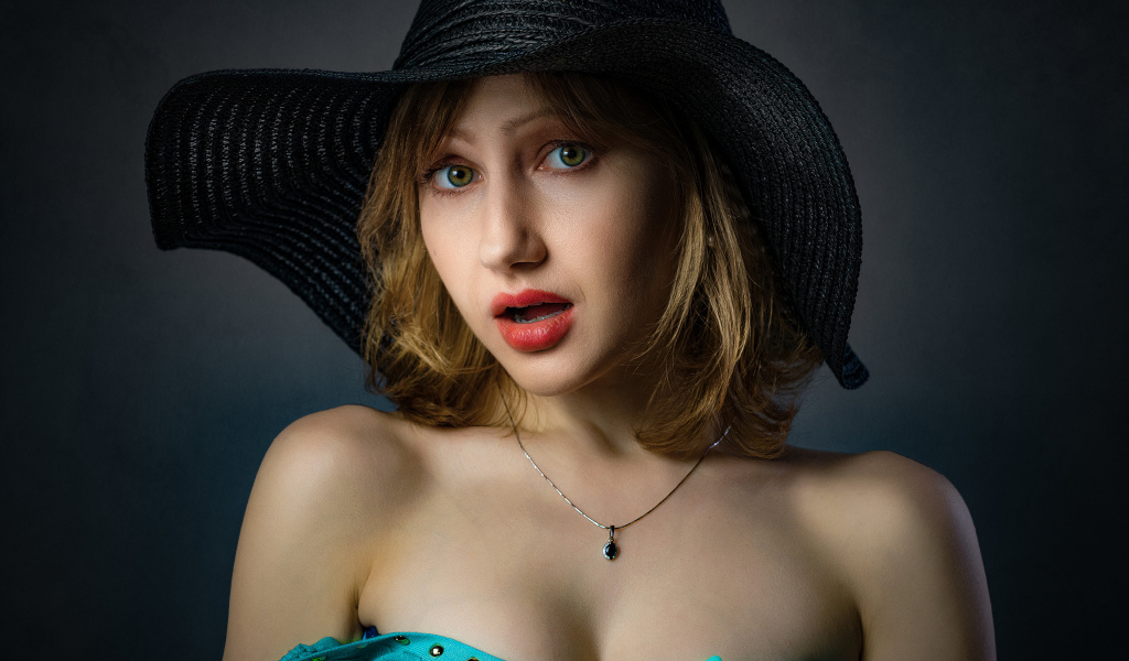 Красивая девушка в большой черной шляпе на сером фоне 