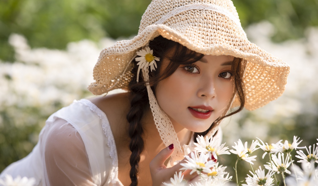 Красивая девушка в шляпе на поле с ромашками 
