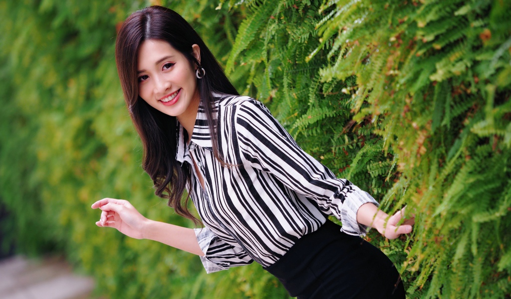 Красивая девушка в полосатой рубашке стоит у растения