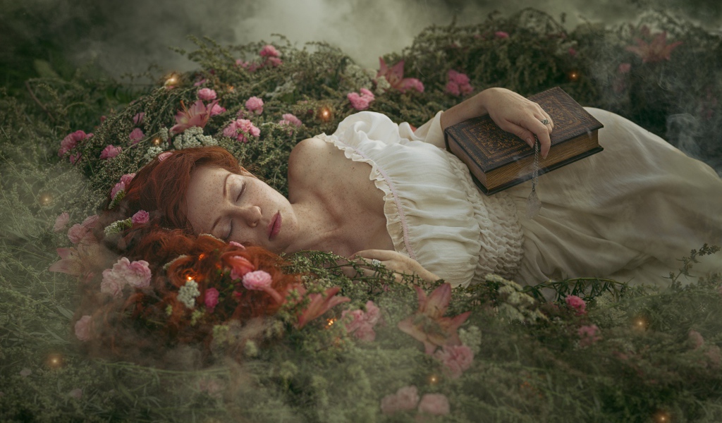 Красивая рыжеволосая девушка спит на земле с книгой