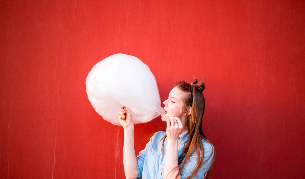 Девушка ест сладкую вату на красном фоне 