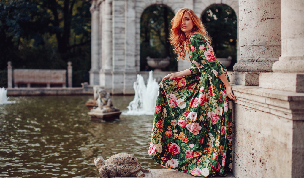 Девушка в красивом цветастом платье у пруда в парке 